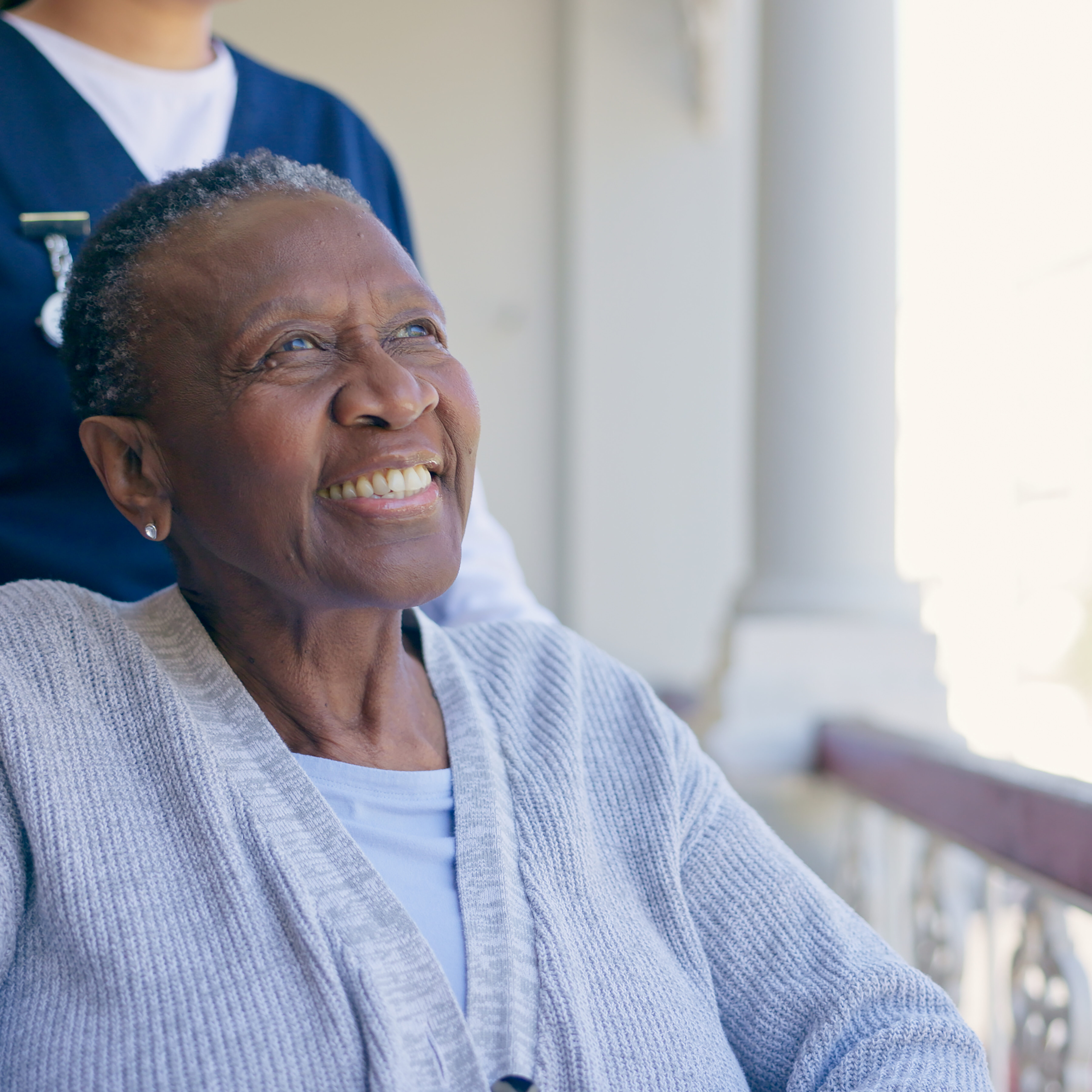 Old woman, wheelchair and nurse outdoor for smile in nature, balcony or elderly wellness. Medical caregiver, black patient and support for person with disability or retirement home, air or sunlight